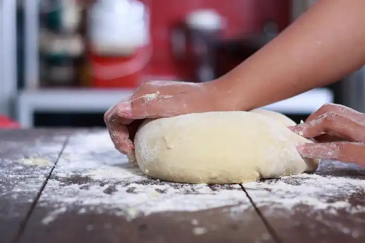 in the kitchen with a blue shirt and cream apron and holding a rolling pin